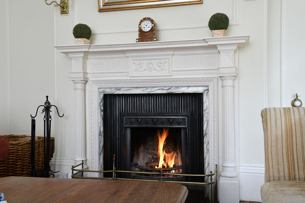 Close-up of a fireplace that has been lit at Lorton House. There is a clock and two small plants decorating the shelf above it.