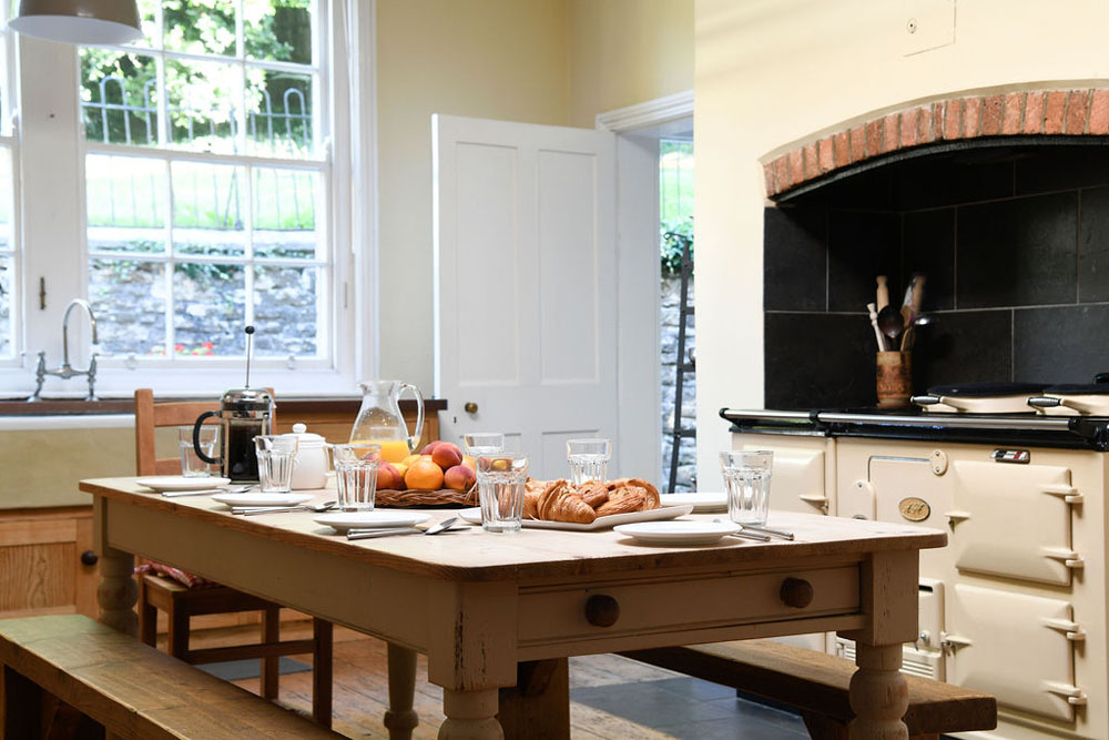 The kitchen at Lorton House. There is an aga on the right, cupboards and shelving on the left and a table that is laid for breakfast in the middle.