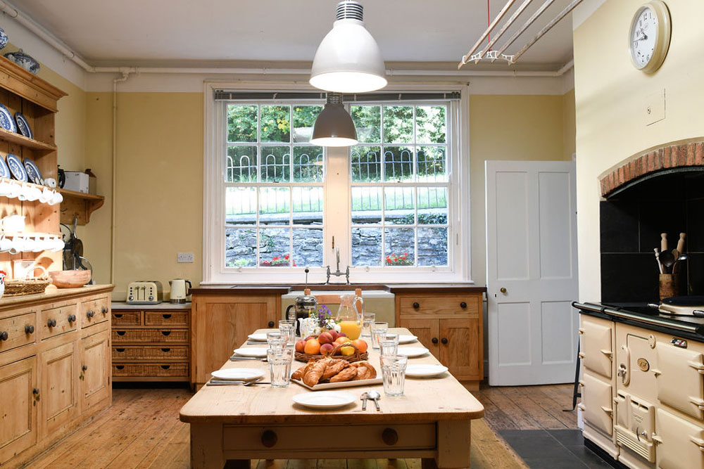 The kitchen at Lorton House. There is an aga on the right, cupboards and shelving on the left and a table that is laid for breakfast in the middle.