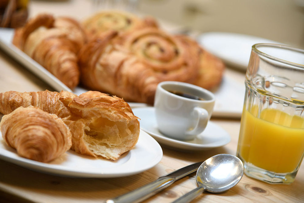 A close-up of croissants, orange juice and coffee on a wooden table.