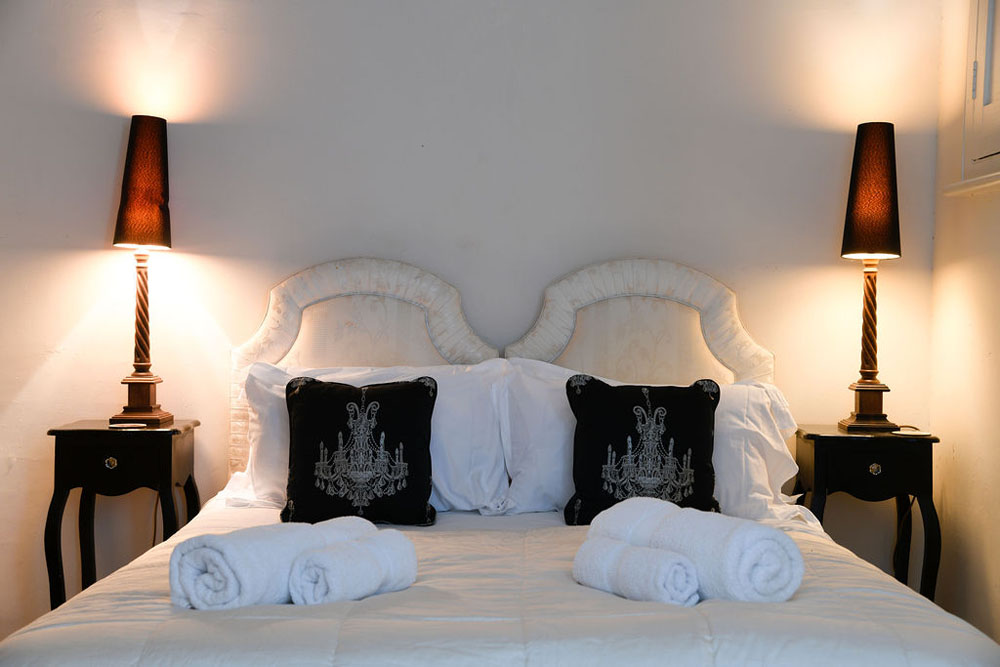 Close-up of a large bed at Lorton House. There are fresh towels laid out and lamps switched on either side of the bed.