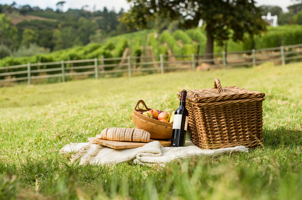 Picnic basket and supplies laid out on a blanket in a meadow