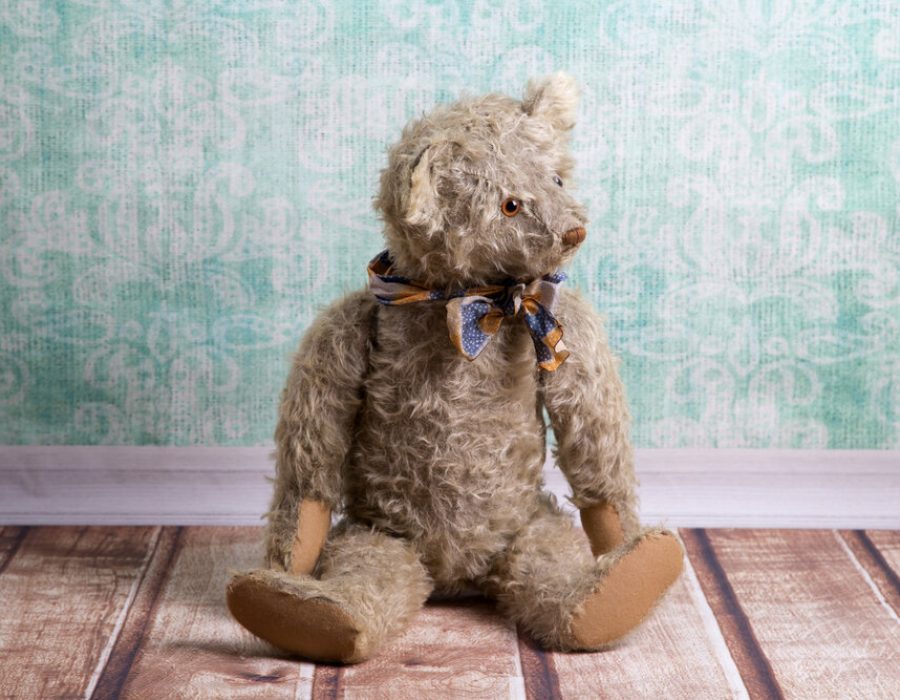 Brown vintage teddy bear wearing a blue and orange ribbon.